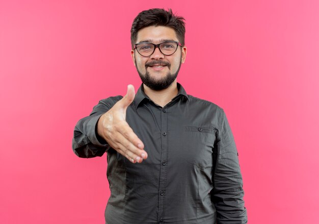 Heureux jeune homme d'affaires portant des lunettes tenant la main isolée sur un mur rose