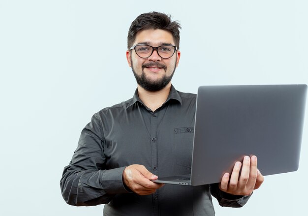 Heureux jeune homme d'affaires portant des lunettes tenant un ordinateur portable isolé sur fond blanc