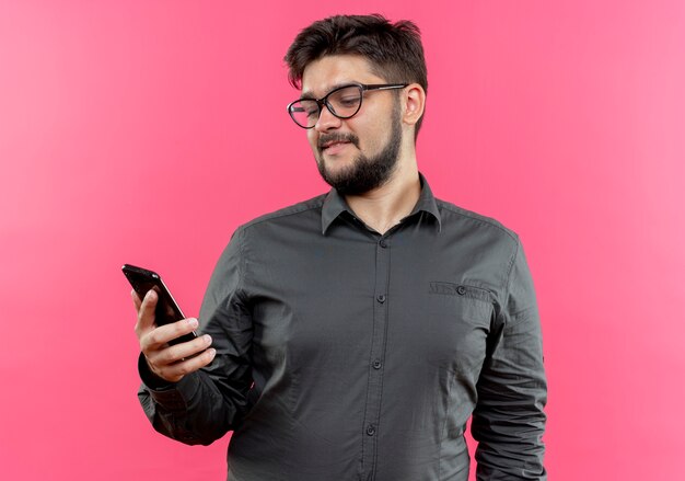 Heureux jeune homme d'affaires portant des lunettes tenant et regardant le téléphone