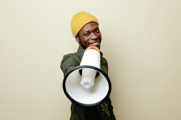 heureux jeune homme afro-américain en chapeau portant une chemise verte tenant un haut-parleur à la caméra isolée sur fond blanc