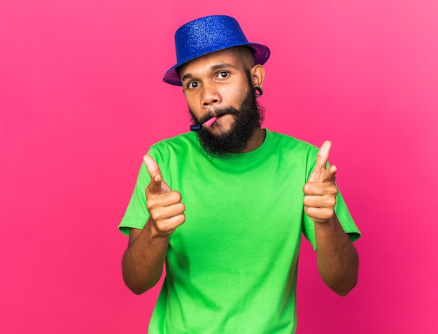 Heureux jeune homme afro-américain portant un chapeau de fête soufflant des points de sifflet de fête à la caméra