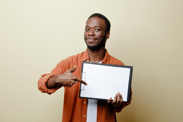 Heureux jeune homme afro-américain tenant et pointe vers le presse-papiers isolé sur fond blanc