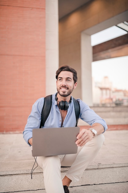 Heureux jeune homme assis sur l&#39;escalier avec un ordinateur portable