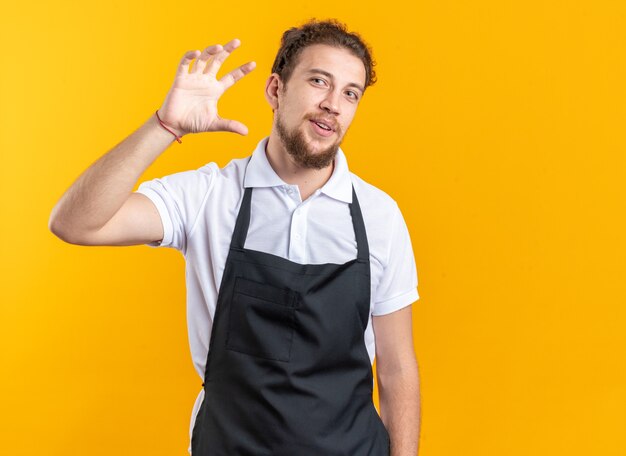 Heureux jeune homme barbier en uniforme montrant la taille isolé sur mur jaune