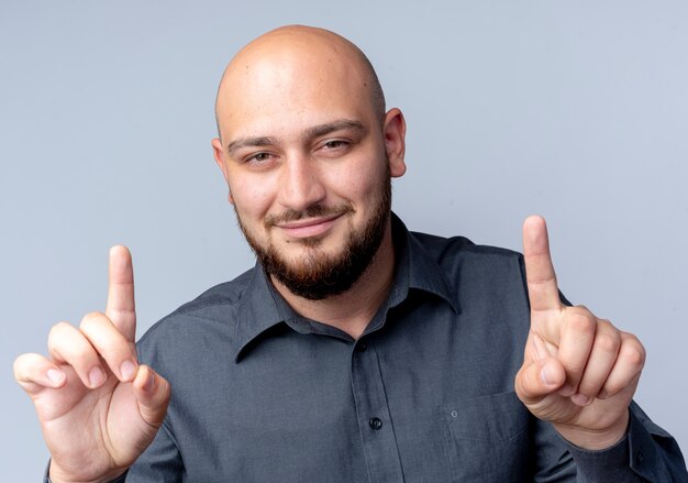 Heureux jeune homme de centre d'appels chauve regardant la caméra et pointant les doigts vers le haut isolé sur fond blanc