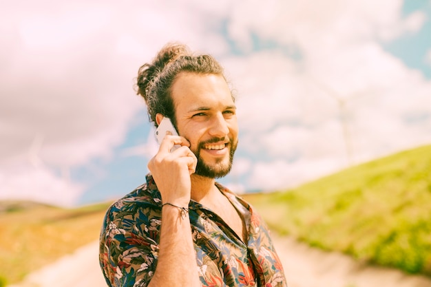 Heureux jeune homme conversant sur smartphone sur la nature