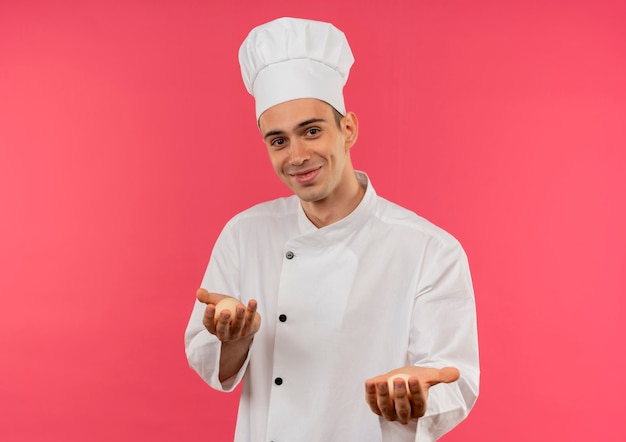 Heureux jeune homme cuisinier portant l'uniforme de chef tenant des oeufs