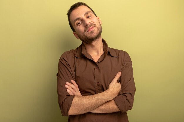 Heureux jeune homme debout avec une posture fermée à l'avant isolé sur mur vert olive