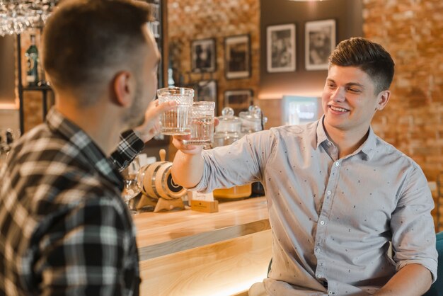 Heureux jeune homme grillage des verres de cocktail au restaurant