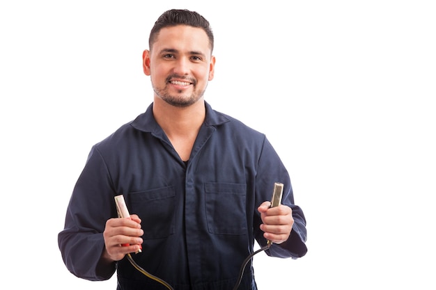 Heureux jeune homme hispanique tenant un couple de bornes de câble de raccordement sur fond blanc