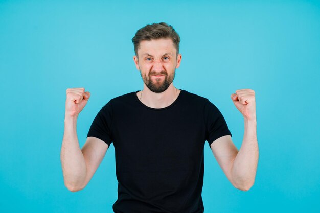 Heureux jeune homme lève les poings sur fond bleu