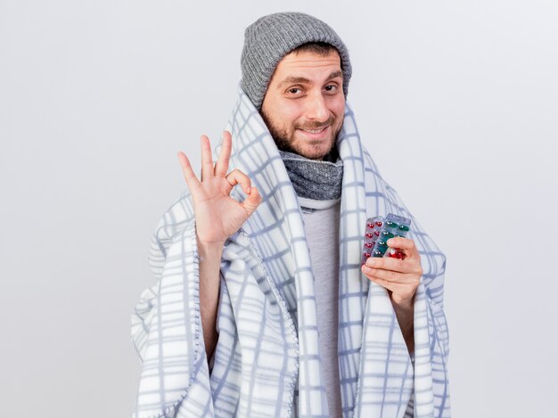 Heureux jeune homme malade portant un chapeau d'hiver et une écharpe enveloppée de pilules à carreaux holding