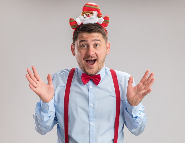 Heureux jeune homme portant des bretelles noeud papillon dans la jante avec santa looking at camera étonné et surpris debout sur fond blanc