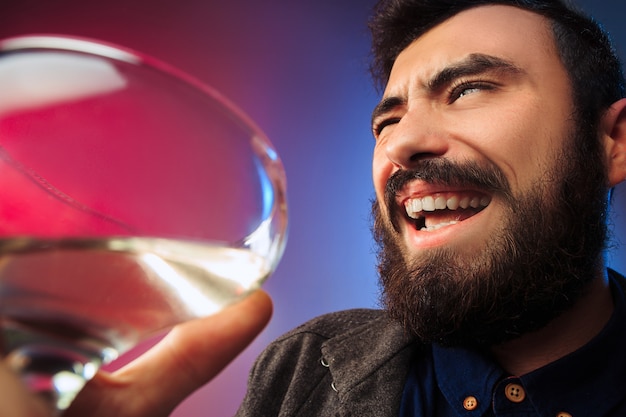 L'heureux jeune homme posant avec un verre de vin. Visage masculin émotionnel. Vue depuis le verre. La fête, Noël, alcool, concept d'événement de célébration