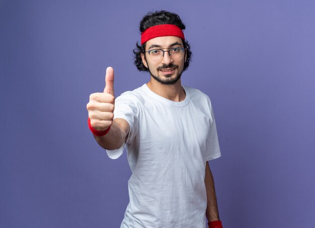 Heureux jeune homme sportif portant un bandeau avec bracelet montrant le pouce vers le haut