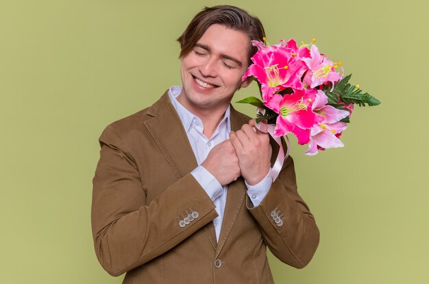 Heureux jeune homme tenant un bouquet de fleurs souriant joyeusement la journée internationale de la femme debout sur le mur vert