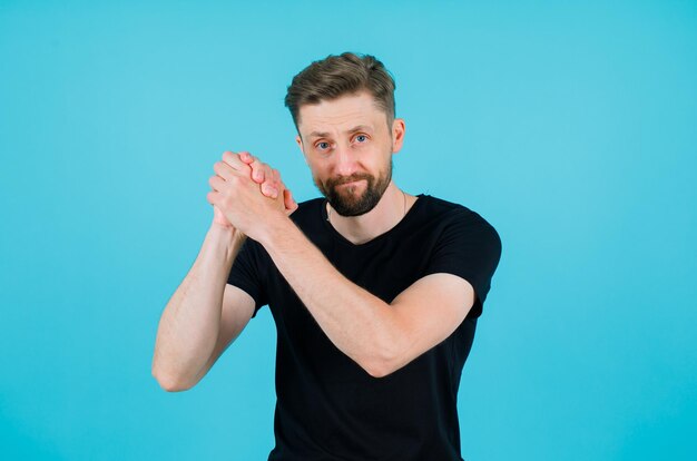 Heureux jeune homme tient les mains ensemble et les lève sur fond bleu