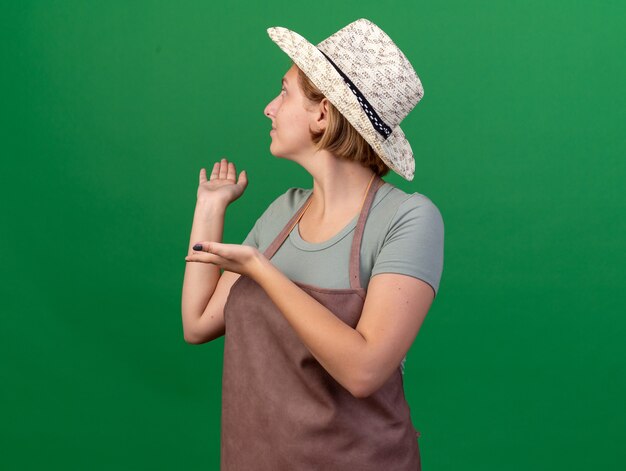Heureux jeune jardinier femme slave portant chapeau de jardinage à la recherche et pointant vers l'arrière sur le vert
