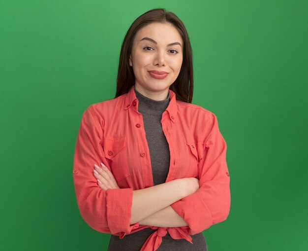 Heureux jeune jolie femme debout avec une posture fermée regardant la caméra isolée sur fond vert avec espace copie