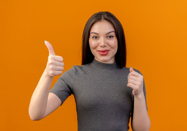 Heureux jeune jolie femme montrant le pouce vers le haut et gardant la main dans l'air isolé sur orange