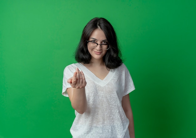 Photo gratuite heureux jeune jolie fille caucasienne portant des lunettes faisant venir ici geste isolé sur fond vert avec espace copie