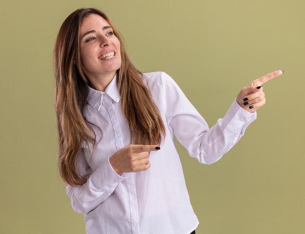 Heureux jeune jolie fille caucasienne regarde et pointe sur le côté sur vert olive