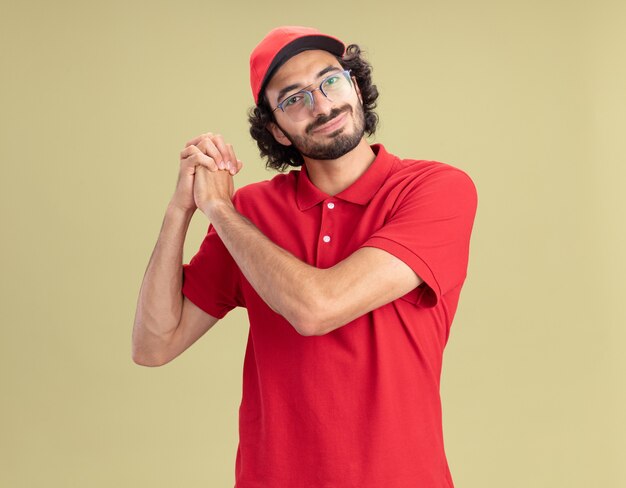 Heureux jeune livreur caucasien en uniforme rouge et casquette portant des lunettes faisant un geste gagnant