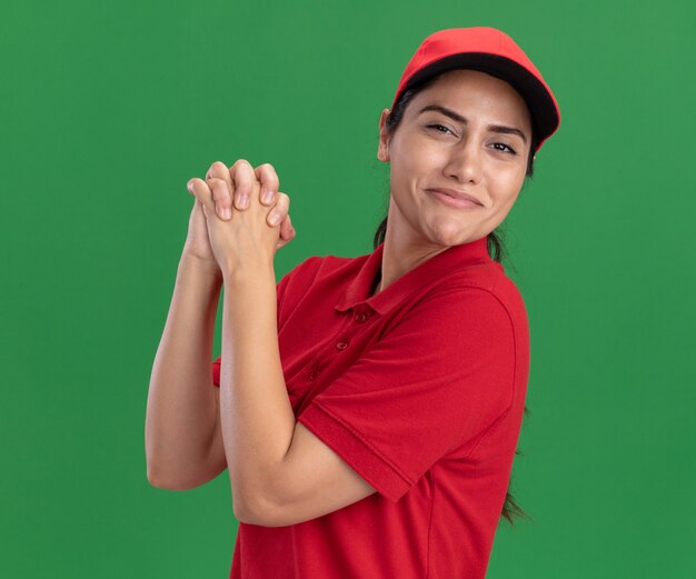 Heureux jeune livreuse portant l'uniforme et une casquette montrant le geste de poignée de main isolé sur un mur vert