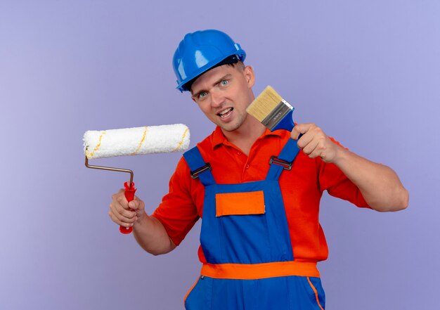 heureux, jeune, mâle, constructeur, porter, uniforme, et, casque sécurité, tenue, rouleau peinture, et, pinceau