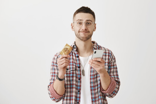 Heureux jeune mec souriant avec des lunettes posant avec son téléphone et sa carte