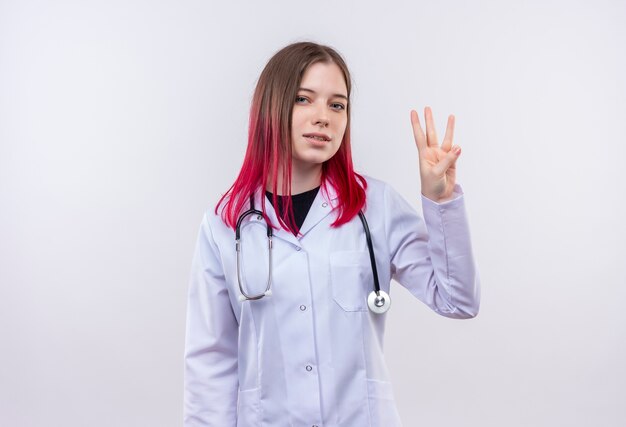 Heureux jeune médecin fille portant une robe médicale stéthoscope montrant trois sur fond blanc isolé