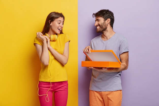 Heureux jeune modèle masculin ouvre la boîte, fait la surprise pour la petite amie le jour de l'anniversaire, montre quelque chose dans le paquet