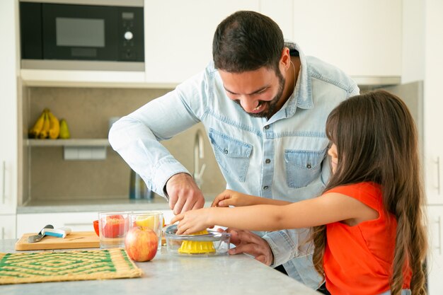 Heureux jeune papa et fille appréciant la cuisine ensemble. Fille et son père pressant du jus de citron au comptoir de la cuisine. Concept de cuisine familiale