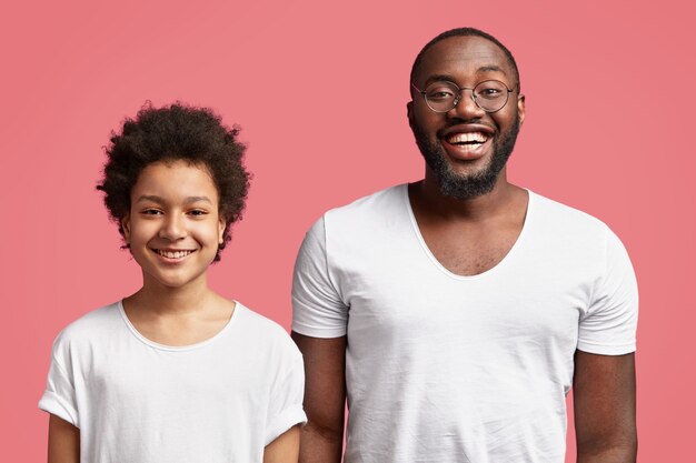 Heureux jeune père se tient étroitement à son petit-fils, étant de bonne humeur, avoir un large sourire, se réjouir de voir des invités, isolé sur un mur rose