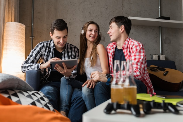 Heureux les jeunes à l'aide de tablette, les étudiants apprennent, s'amusent, font la fête entre amis à la maison, entreprise hipster ensemble, deux hommes une femme, souriant, positif, éducation en ligne, écouter de la musique