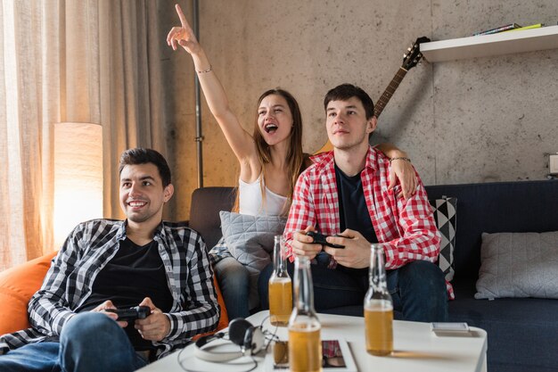 Heureux les jeunes jouer à des jeux vidéo, s'amuser, faire la fête entre amis à la maison, entreprise hipster ensemble, deux hommes une femme, souriant, positif, détendu, émotionnel, rire, compétition