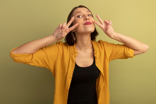 Heureux jolie femme caucasienne gestes signe de la main de la victoire avec deux mains sur vert olive