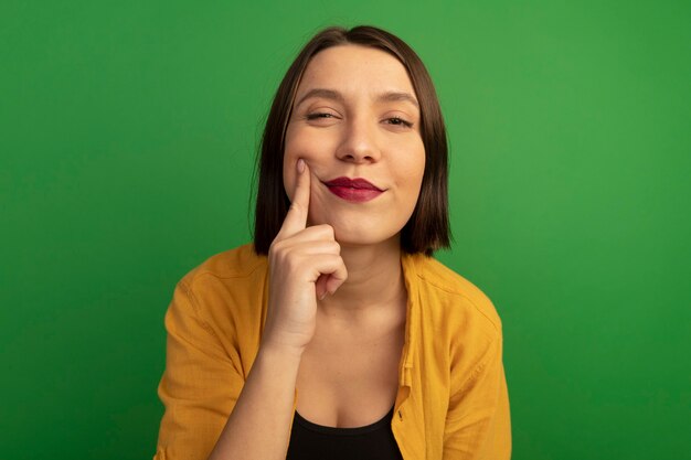 Heureux jolie femme met le doigt sur la joue isolé sur mur vert