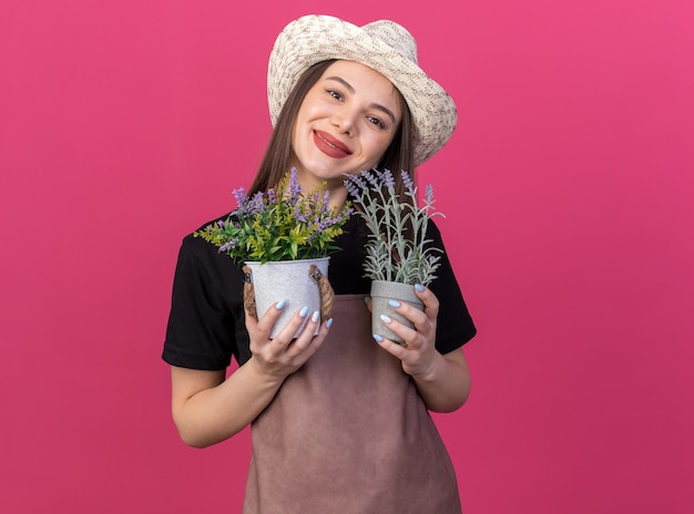 Heureux Jolie Jardinière Caucasienne Portant Un Chapeau De Jardinage Tenant Des Pots De Fleurs Isolés Sur Un Mur Rose Avec Espace Pour Copie