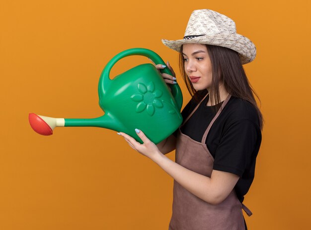 Heureux jolie jardinière caucasienne portant un chapeau de jardinage tenant et regardant un arrosoir