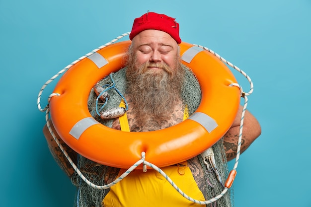 Heureux joyeux pêcheur barbu se tient avec les yeux fermés porte bouée gonflée orange passe du temps libre sur des poses de bateau de pêche