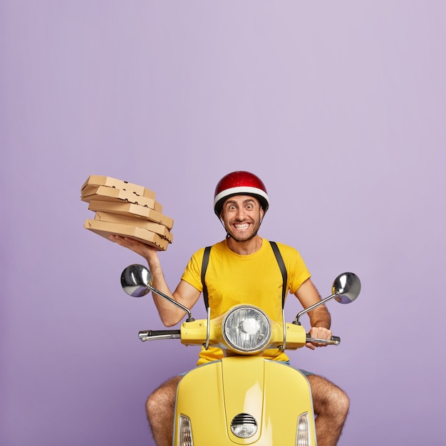 Heureux livreur conduisant un scooter jaune tout en tenant des boîtes à pizza
