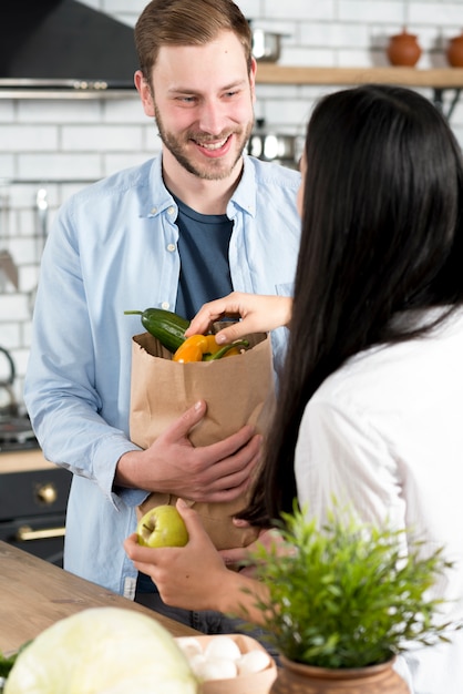 Heureux mari debout cuisine tenant un sac d&#39;épicerie brun