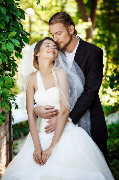 Heureux mariés souriant avec les yeux fermés, embrassant dans le parc.