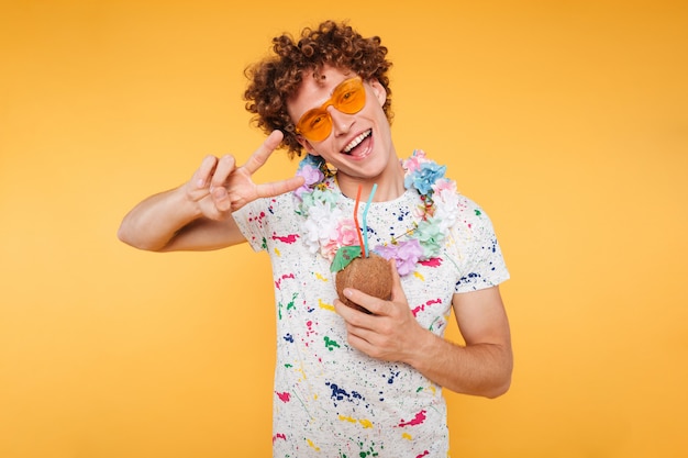 Heureux mec attrayant à lunettes de soleil tenant un cocktail de noix de coco