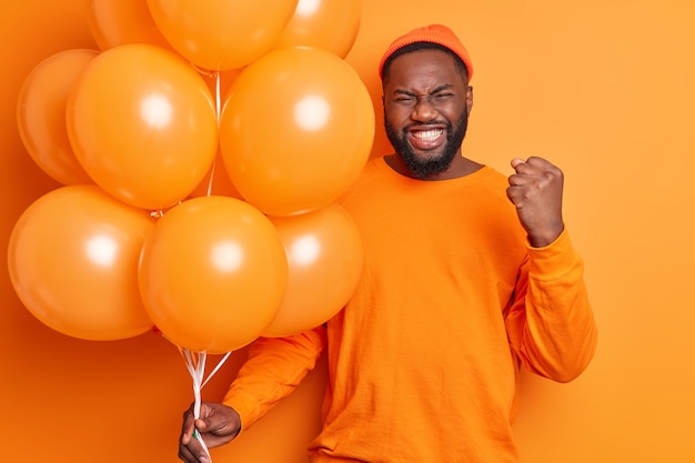 Heureux mec barbu à la peau sombre émotionnelle serre le poing et les dents célèbre l'obtention de la promotion passe du temps libre à la fête