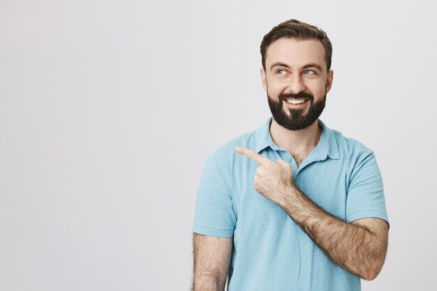 Heureux mec caucasien souriant avec barbe pointant vers la gauche