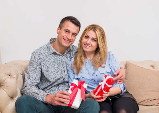 Heureux mec embrassant une femme souriante avec des cadeaux et assis sur un canapé