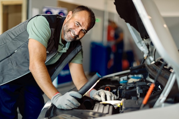 Heureux mécanicien d'âge moyen travaillant dans un atelier de réparation automobile et regardant la caméra