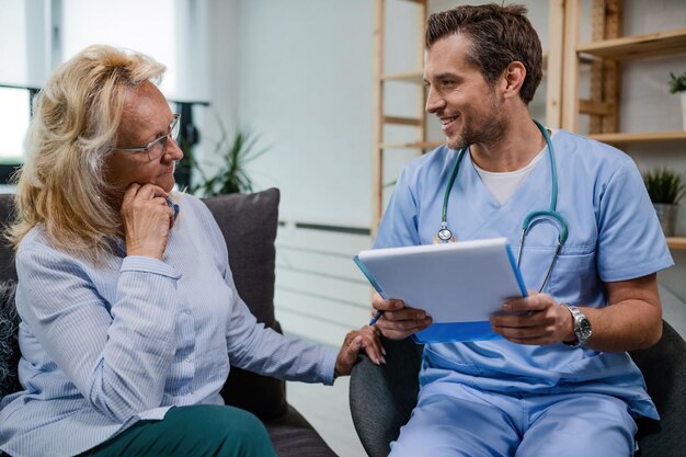 Heureux médecin communiquant avec une femme âgée au sujet de documents médicaux lors d'une visite à domicile